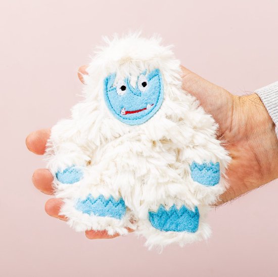 Een zachte, witte knuffel Yeti met blauwe voeten, handen en gezicht met rode mond en ogen, zittend in een hand.