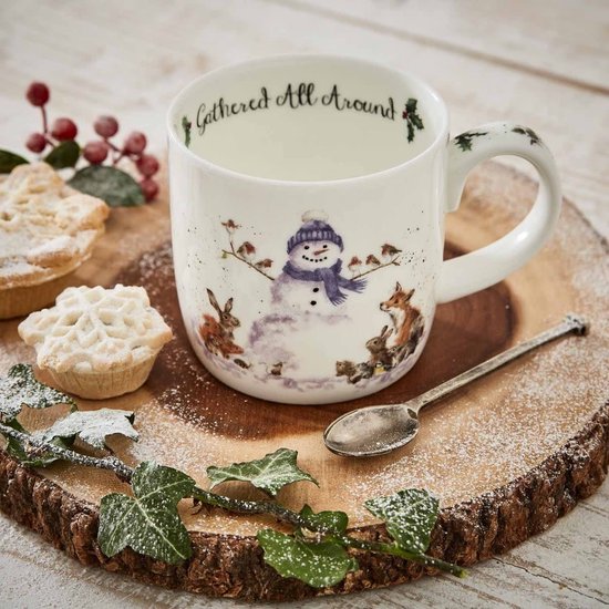 Witte mok met opdruk van een sneeuwpop met vogeltjes, een vos, konijn en eekhoorn. Staat op een houten schijf met kerstkransjes en bestek.