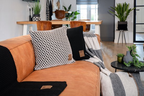Zwarte en witte kussens met stippen en gebreide texturen op een bruine bank, met gestreepte plaids.