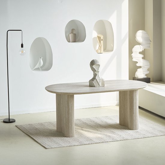 Een ovaal, lichtgrijze eettafel met gecanneleerde poten op een geblokt vloerkleed in een minimalistische setting.