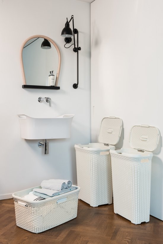 Badkamer met witte wasmanden en een witte wasmand met handvatten, gevuld met handdoeken. Links een witte wasbak met spiegel.