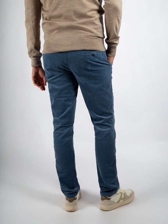 Man in beige trui en blauwe corduroy chino broek, rug gezien.