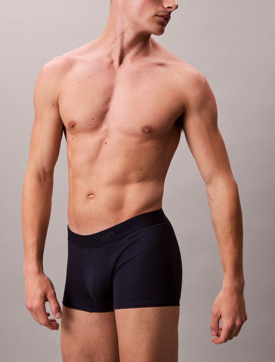 Man met gespierd bovenlichaam in donkerblauwe Calvin Klein boxershort, staand.