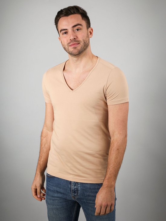 Een man in een beige v-hals t-shirt en spijkerbroek.