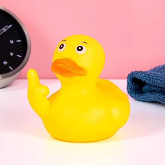 Gele badeend met oranje snavel die een middelvinger opsteekt, naast een wekker en handdoek.