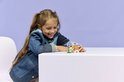 Une fille en veste en jean est assise à une table, regardant un hamster LEGO avec une fleur.