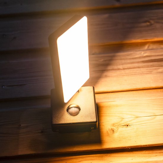 Zwarte wandlamp met sensor, verlicht houten planken met warm licht.