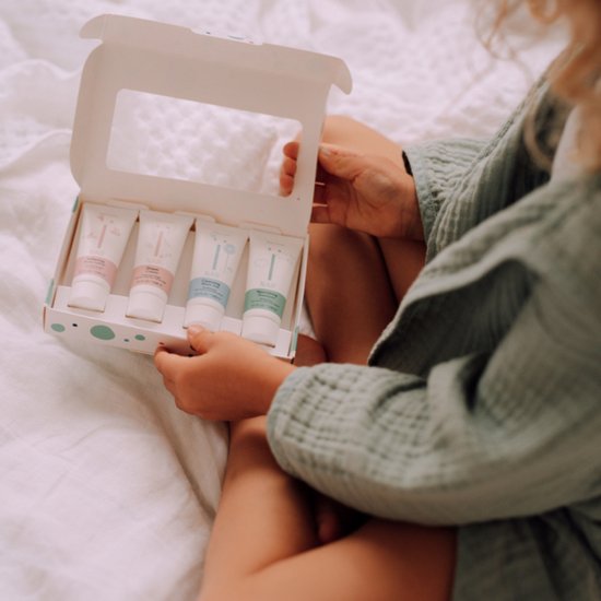 Een kind houdt een Naïf miniset babyverzorging vast. De set bevat vier tubes: Wasgel, Shampoo, Baby Crème en Zinkcrème.