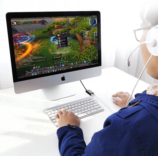 Zwarte UGREEN USB geluidskaart adapter aangesloten op iMac, man speelt online game.