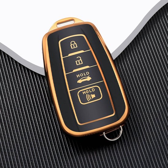 Zwarte autosleutelhoes met gouden rand en 4 knoppen, liggend op een zwarte ondergrond.