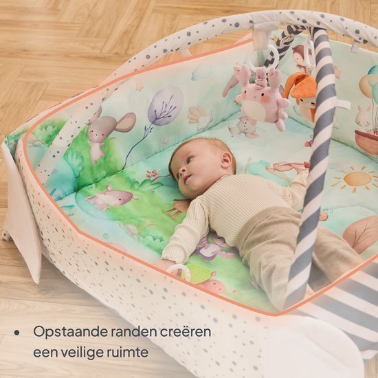 Een baby liggend op een speelmat met zachte opstaande randen en speelgoed. De mat heeft afbeeldingen van dieren en natuur.