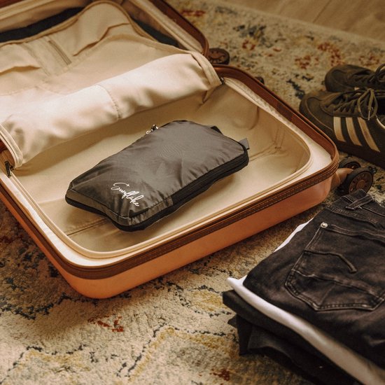 Grijze, opgevouwen Sunflake packing cube in een open, roze koffer. Naast de cube liggen kleding en sneakers.