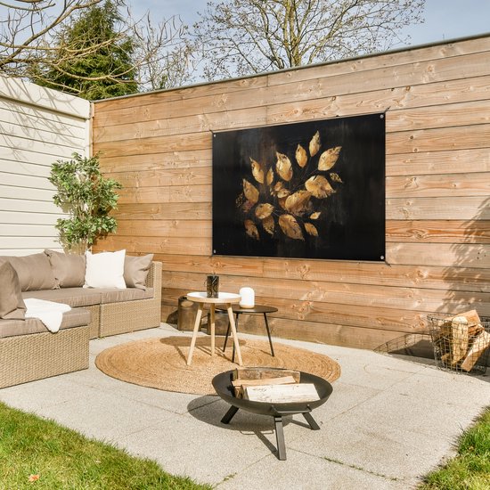 Feuilles dorées sur fond sombre, suspendues à une clôture en bois à côté d'un salon de jardin, dans le jardin.