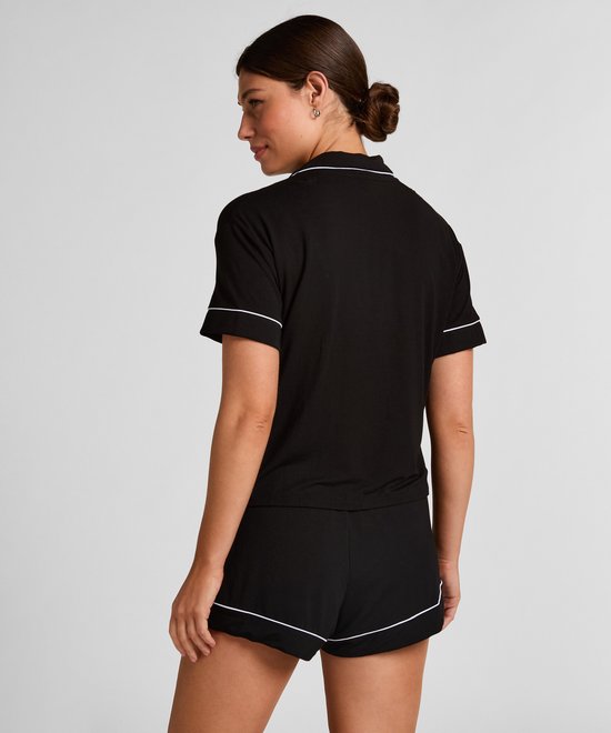 Model van achteren gezien, draagt een zwart pyjamashirt met witte biezen.
