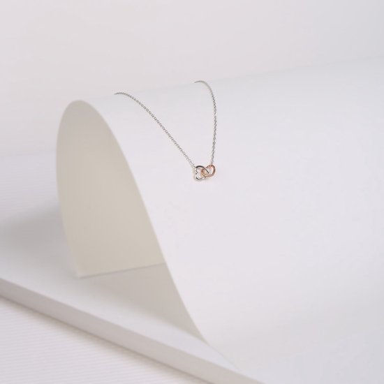 Zilverkleurige ketting met twee in elkaar grijpende hartjes, los op een witte achtergrond met een subtiele schaduw.
