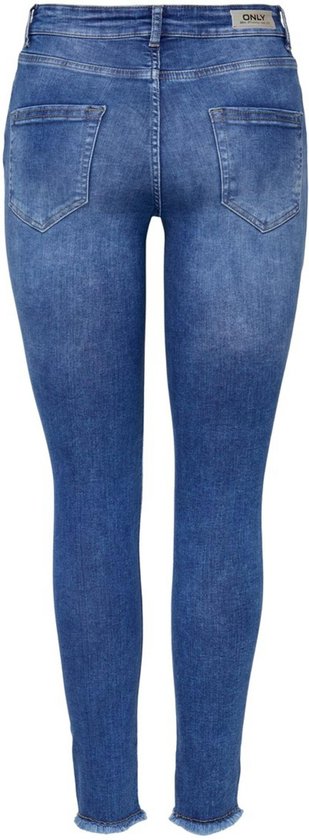 Achterkant van een vrouw in een blauwe skinny jeans met rafelige zoom, gedragen met zwarte pumps.