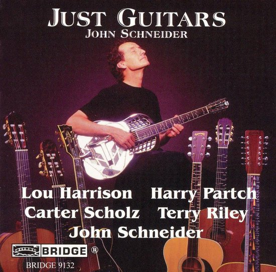 John Schneider speelt op een resonatorgitaar, omringd door akoestische gitaren. Tekst: Just Guitars John Schneider.