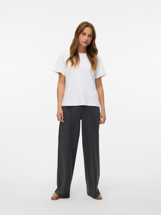 Model in een donkergrijze broek met wijde pijpen en een witte top. De broek heeft een hoge taille en verticale naden.