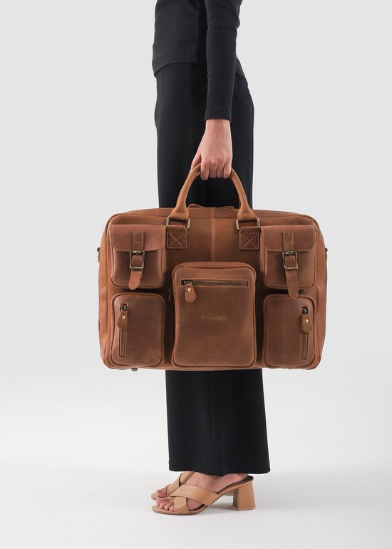 Een vrouw met een zwarte top en broek draagt een grote bruine leren aktetas met meerdere vakken en handvatten.
