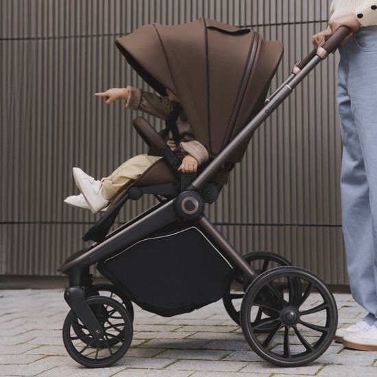 Een vrouw duwt een bruine kinderwagen met een baby die naar buiten wijst.