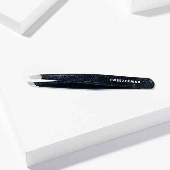 Zwarte glitter Tweezerman pincet met schuine punten op een witte kubus.
