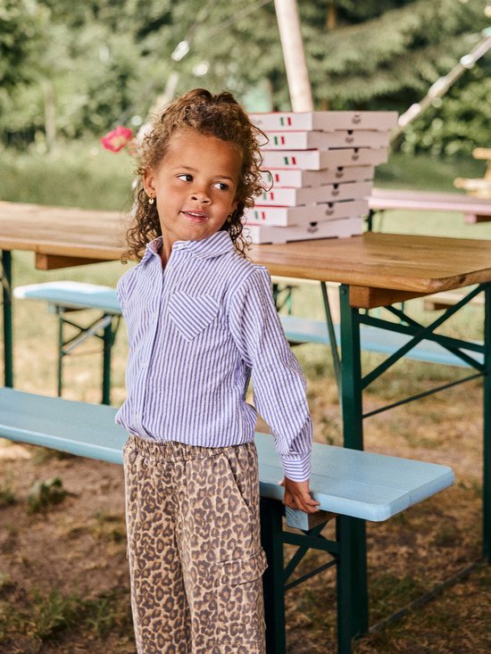 Meisje met krullend haar in een blauw-wit gestreepte blouse en luipaardprint broek.