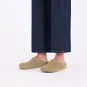 Voeten in spijkerbroek en beige suède Birkenstock Boston slippers, bekeken vanaf de voorkant.