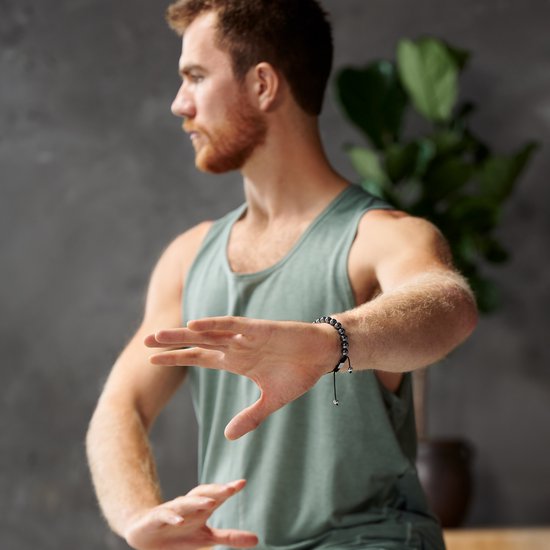 Een man met een groene tanktop draagt een hematiet kralen armband om zijn pols tijdens een tai chi pose.