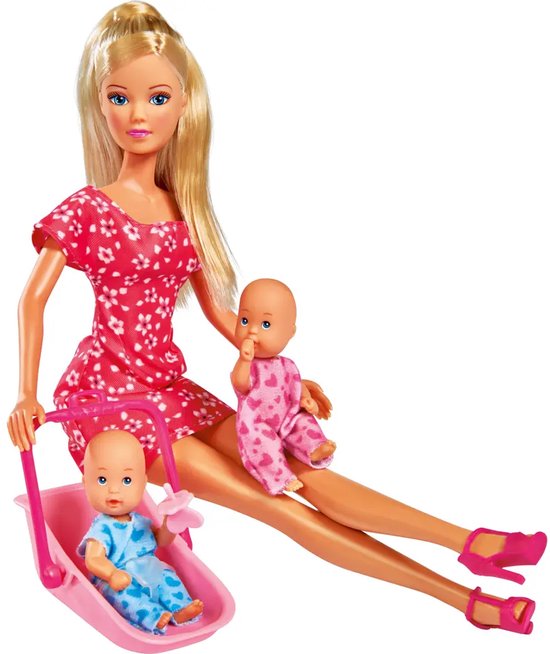 Pop met blonde haren draagt roze jurk met witte bloemen, houdt twee baby's vast. Eén baby in draagzak, de ander in roze wieg.
