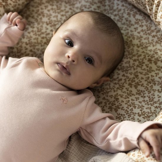 Baby in een lichtroze longsleeve shirt met fijne ribbels en geborduurd logo. Ze ligt op een bloemetjesstof.