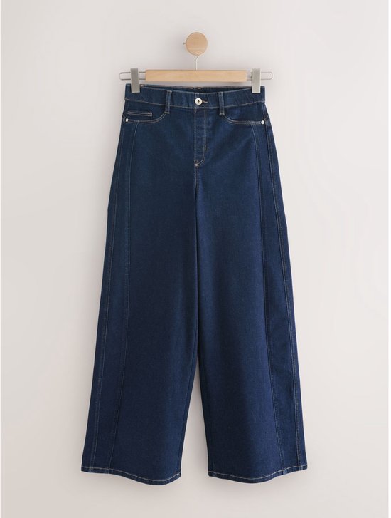 Donkerblauwe, wijde spijkerbroek met hoge taille, hangend aan een kledinghanger.