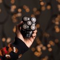 Een hand met kersttrui houdt een zwart Remington hoofdscheerapparaat vast met lichten op de achtergrond.