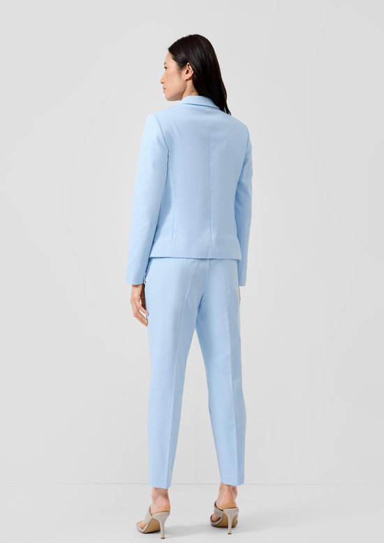 Vrouw draagt lichtblauwe blazer en broek, zicht van achteren.