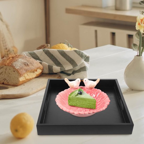 Zwart dienblad met een stuk groene taart met blauwe bes op een roze schaal met vogeldecoraties.