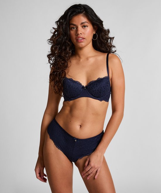 Model met krullend haar draagt een donkerblauwe kanten beugelbeha en bijpassend bikinislipje.