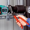 Hand met Knipex Alligator waterpomptang die een verwarmingsbuis klemt, naast een manometer.
