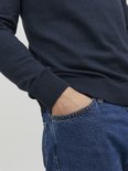 Donkerblauwe gebreide trui met coltrui en een hand in de jeanszak.