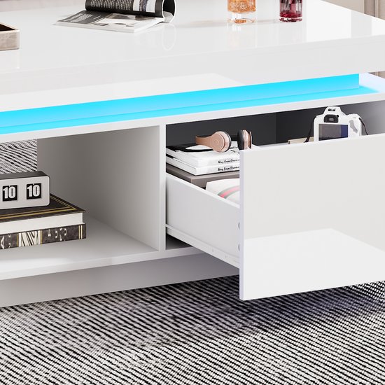 Gedeeltelijk geopende lade van de witte hoogglans salontafel, met opbergruimte voor koptelefoons en boeken, met blauwe LED-verlichting.