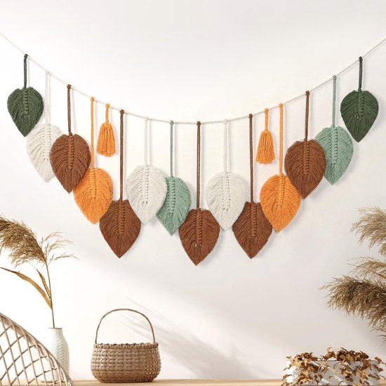 Guirlande macramé feuille verte, blanche, marron et orange, suspendue à une corde au-dessus d'un panier et de plantes séchées.