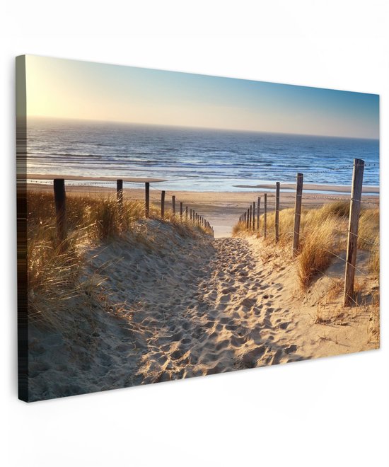 Zandpad met houten palen en duingras leidt naar een strand en de zee bij zonsondergang.