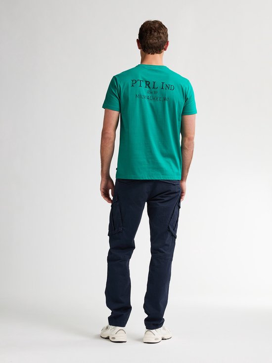 Man met rug naar voren, draagt een groene t-shirt met tekst en donkerblauwe cargobroek.