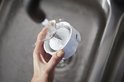 Hand die de blenderbeker met messen onder de kraan afspoelt. Witte beker met metalen mesjes.