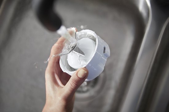 Hand die de blenderbeker met messen onder de kraan afspoelt. Witte beker met metalen mesjes.