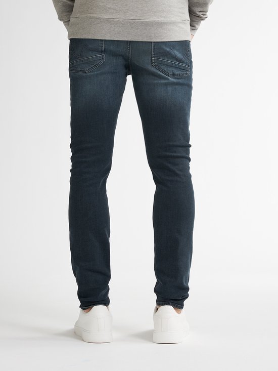 Man in grijze sweater en donkerblauwe slim fit jeans, van achteren gezien.