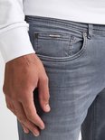 Detail van de voorkant van een grijze jeans met een klein metalen logo bij de zak.