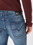 Close-up van de achterkant van een lichtblauwe jeans met een zwart label "TTD TOM TAILOR DENIM BRAND".