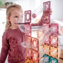 Een jong meisje bouwt met pastelkleurige Connetix-tegels en transparante buizen een hoge glijbaan.