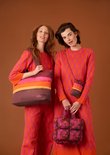Twee modellen in oranje en roze outfits. Het linker model draagt een gestreepte tas, het rechter model een
schoudertas en een kleine handtas.