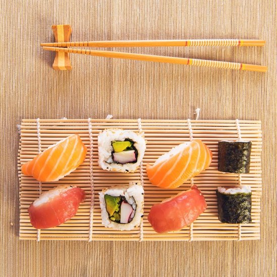 Verschillende sushirollen en stukken zalm en tonijn op een bamboe mat, met eetstokjes.
