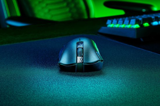 Een zwarte draadloze gamingmuis op een zwart gamingmuismat, met een verlicht toetsenbord op de achtergrond.